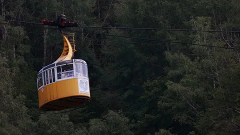 Yellow cable car transporting passengers over green mountain forest 库存影片 335296120