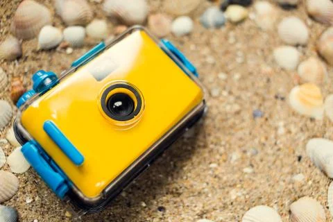 Yellow camera lying on sand at the beach Stock Photos