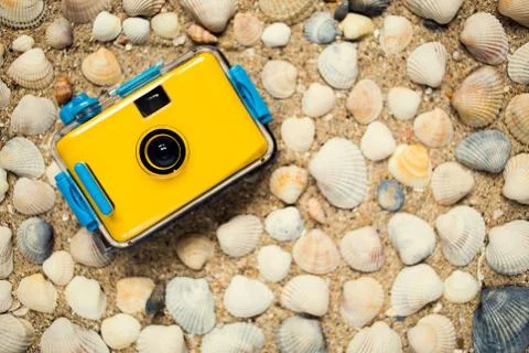 Yellow camera lying on sand at the beach Stock Photos
