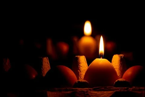 A yellow candle in the shape of an egg in the dark on a tray with chicken egg Stock Photos