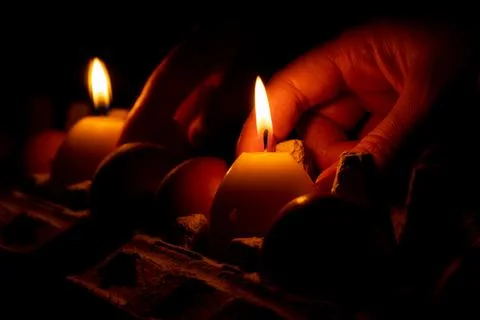 A yellow candle in the shape of an egg in the hand of a girl in the dark on a Stock-Fotos