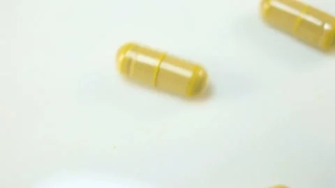 Yellow capsules with a biological Supplement inside roll down the white backgrou Stock Footage 144642835
