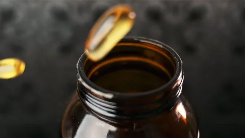 Yellow capsules with vitamin D3 fall randomly into the neck of the bottle, some Stock Footage 262103633