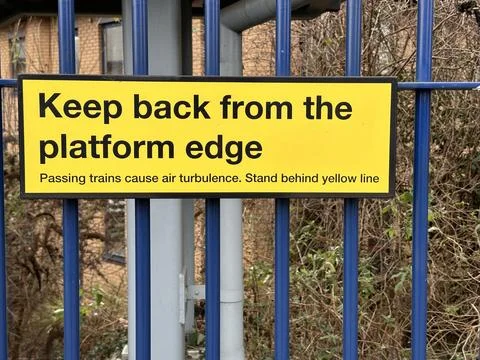 Yellow caution sign keep back from platform edge on a metal fence Stock Photos