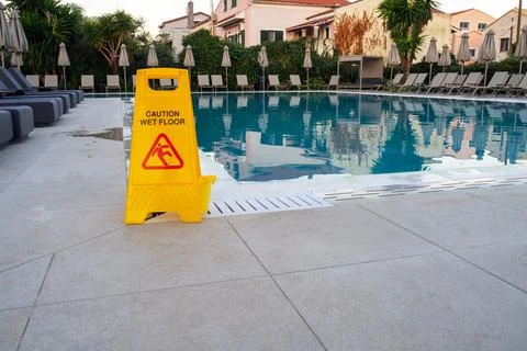 A yellow caution sign is placed in front of a swimming pool Stock Photos