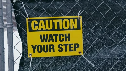 A yellow caution sign reading Caution Watch Your Step mounted on a chain-link 스톡 동영상 322657598