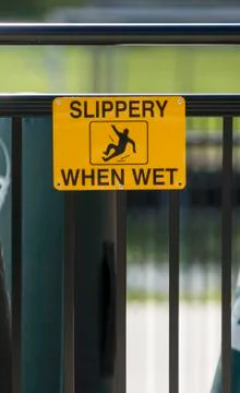 Yellow caution sign warns surface is "Slippery When Wet" Stock Photos