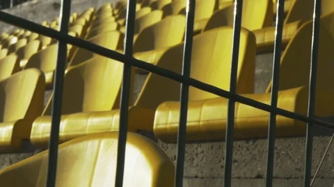 Yellow chairs in an empty stadium behind a metal fence. Canceled match, game. Видео 88428461