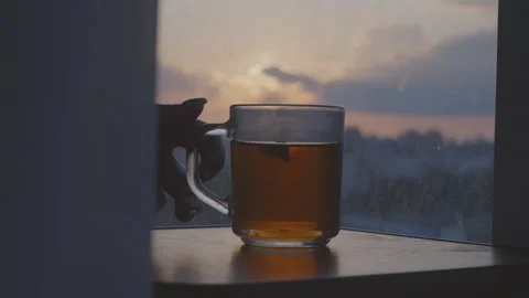 Yellow chamomile flower tea on clear glass mug with tea on windowsill, sunset Stock Footage 270491063
