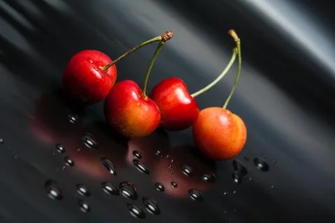 Yellow cherry on black reflective background with water droplets Stock Photos