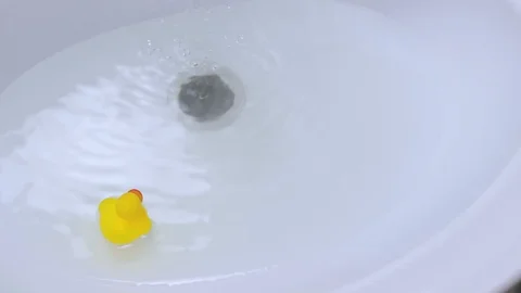 Yellow classical rubber duck floats in clean water in white ceramic bathroom sin Stock Footage 128881672