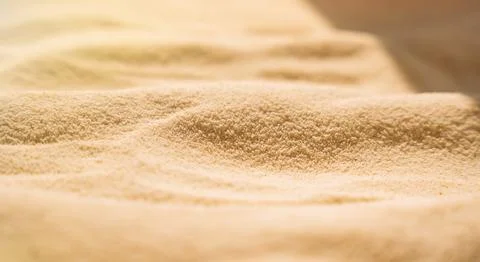 Yellow clean sand with wavy patterns under sunlight Stock Photos