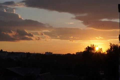 Yellow clouds in the sky at sunset over houses in the urban landscape in summ Foto stock