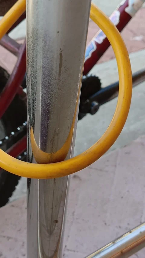 Yellow combination lock for the bicycle. Bicycle fastened to a metal pole with a Video stock 318356301