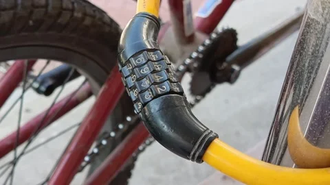 Yellow combination lock for the bicycle. Bicycle fastened to a metal pole with a Stock Footage 318356325