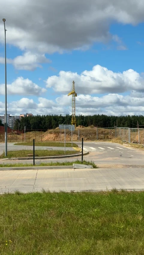 Yellow construction crane at fenced development site with dirt mounds  Video stock 343405803
