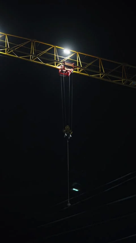 Yellow construction crane jib and hook illuminated against night sky. Stock Footage 342371394
