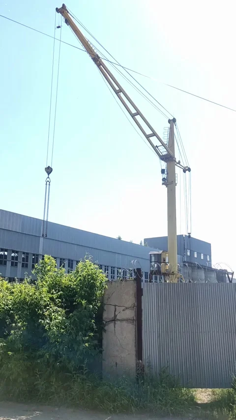 Yellow construction crane rising behind industrial building under bright sky Stock Footage 337179651