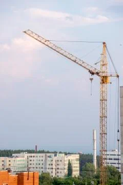 Yellow construction crane on sky background near the multi-storey building Stock Photos