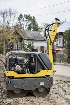 A yellow construction machine sits at a road work site in a small town. The m Stockfoto's