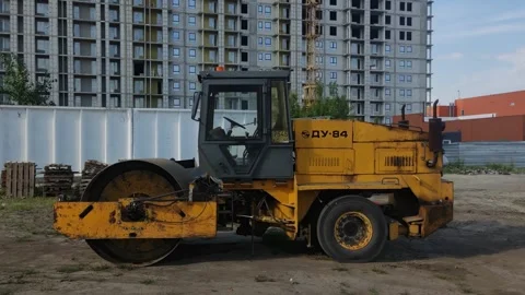 A yellow construction road roller parked near a building site. Stock Footage 339349311