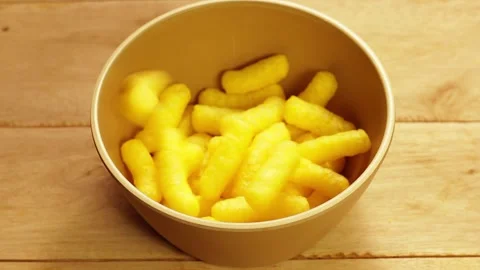 Yellow corn sticks being poured into a brown bowl on a rustic wooden table... Stock Footage 338212368