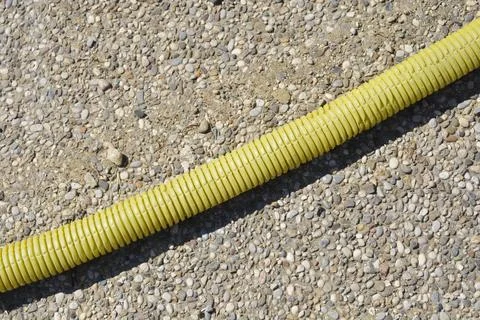 Yellow corrugated plastic pipe on pebble ground Stock Photos