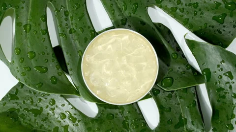 Yellow Cosmetic cream with rotation on background of tropical leaves Monstera Stock Footage 169924853