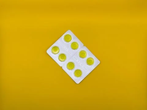 Yellow cough tablets in silver packaging on yellow background, top view Foto stock