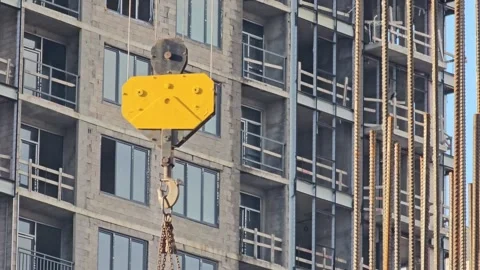 Yellow crane hook block with chain against the facade of an unfinished building Stock Footage 297614036