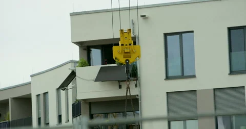 Yellow crane hook lifting loads in front of modern residential building facade Video stock 329680139