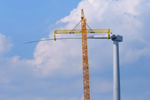 Yellow crane tower placing windmill blade with background of blue sky Stock Photos