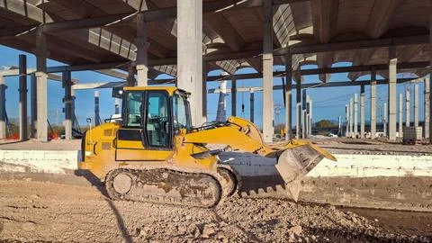 Yellow crawler loader working at a large concrete building construction site. Stock Photos