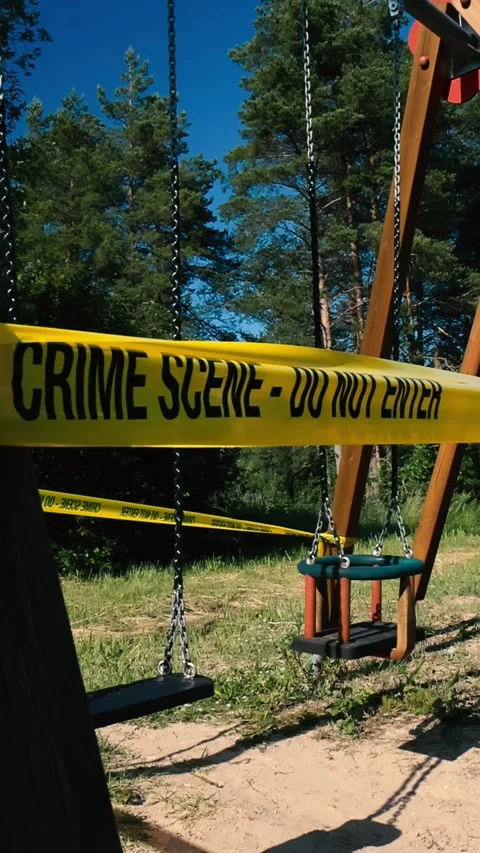 Yellow crime scene tape in front of two empty swings swinging at a sunny summer Stock Footage 312335253