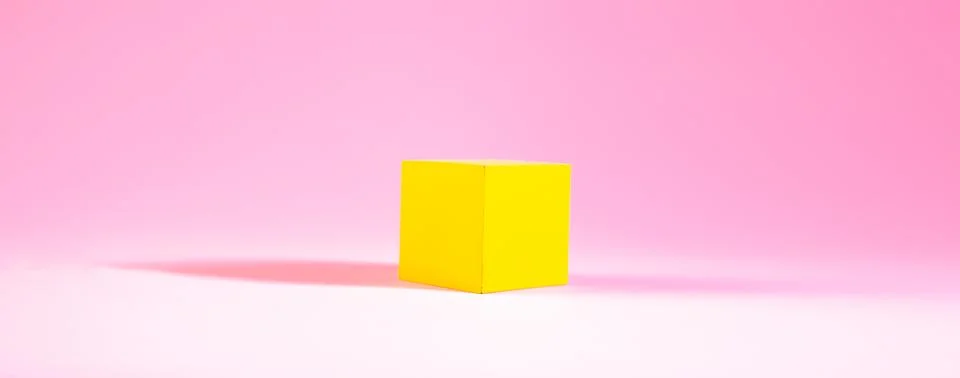 Yellow cube in the shape of a cube on a pink background. Stock Photos