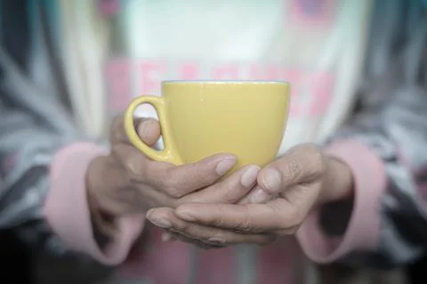 A yellow cup of coffee in a woman's hand 库存照片