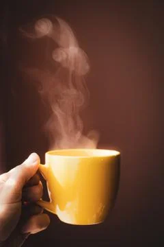 Yellow cup with hot streaming tea drink in hand Stock Photos