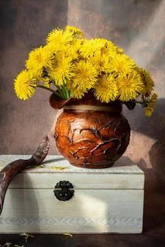 Yellow dandelions in a rustic clay pot resting on a vintage white wooden box. Stock Photos