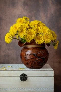 Yellow dandelions in a rustic clay pot resting on a vintage white wooden box. Stock Photos