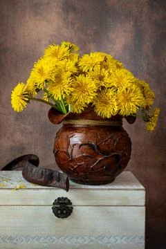 Yellow dandelions in a rustic clay pot resting on a vintage white wooden box. Stock-Fotos