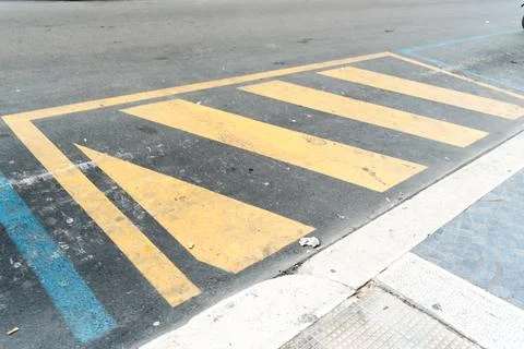 Yellow diagonal hatched road marking painted on dark asphalt beside a blue Stock Photos