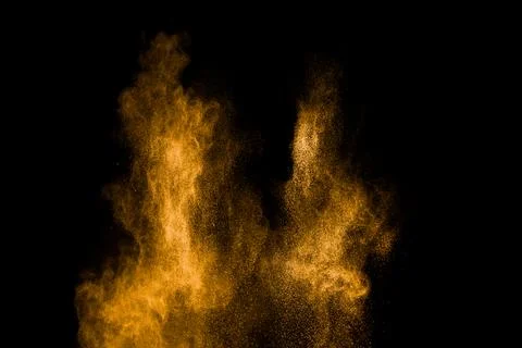 Yellow dust particles explosion on black background.Yellow powder splash. Stock Photos