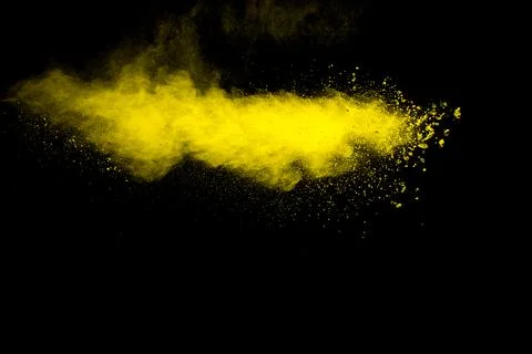 Yellow dust particles explosion on black background.Yellow powder splash. Stock Photos