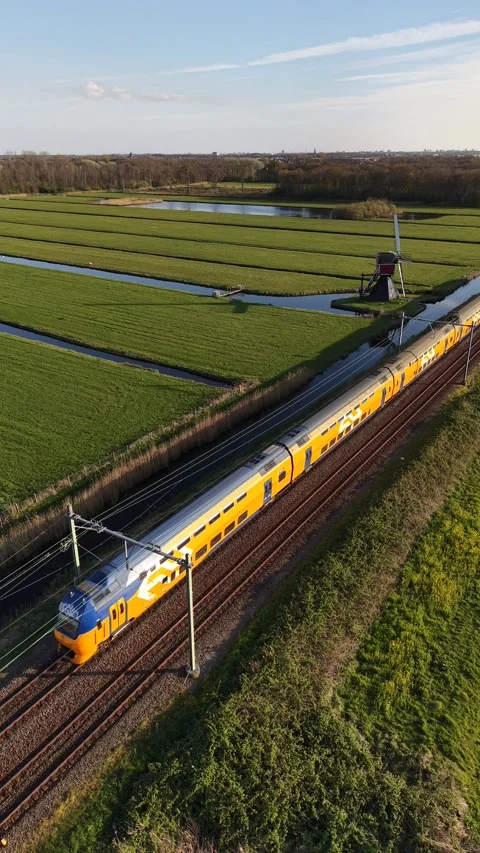 Yellow Dutch Train Passing Windmill and Green Fields -vertical 4K Aerial footage Stock Footage 332815310