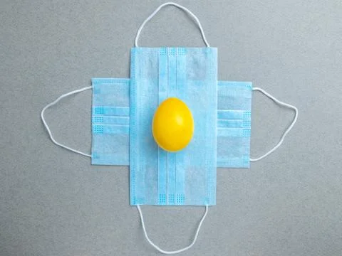 Yellow easter egg lies on blue medical masks on a gray background. Stock Photos