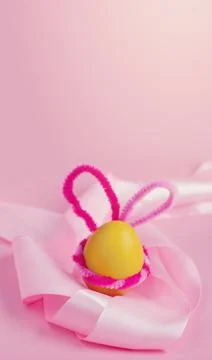 A yellow Easter egg with pink bunny ears lies on a satin ribbon Stock Photos