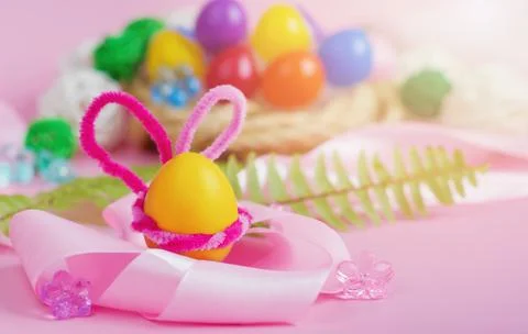 A yellow Easter egg with pink bunny ears and a satin ribbon in the foreground Stock Photos