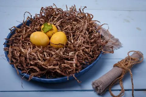 Yellow Easter eggs in brown nest on blue wooden background, close up shot Stock Photos
