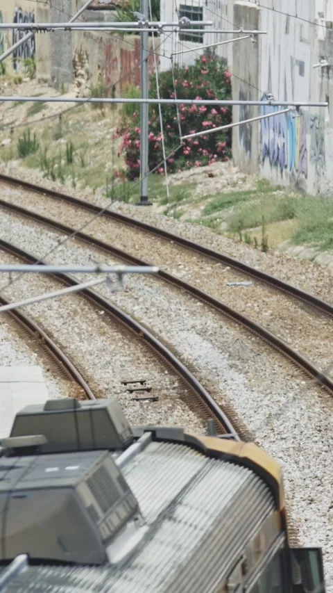 Yellow electric passenger train passing a sunny urban railway station Stock Footage 329472460