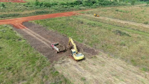 Yellow excavator loading truck on a rectangular farmland plot with red soil. Video stock 309080221